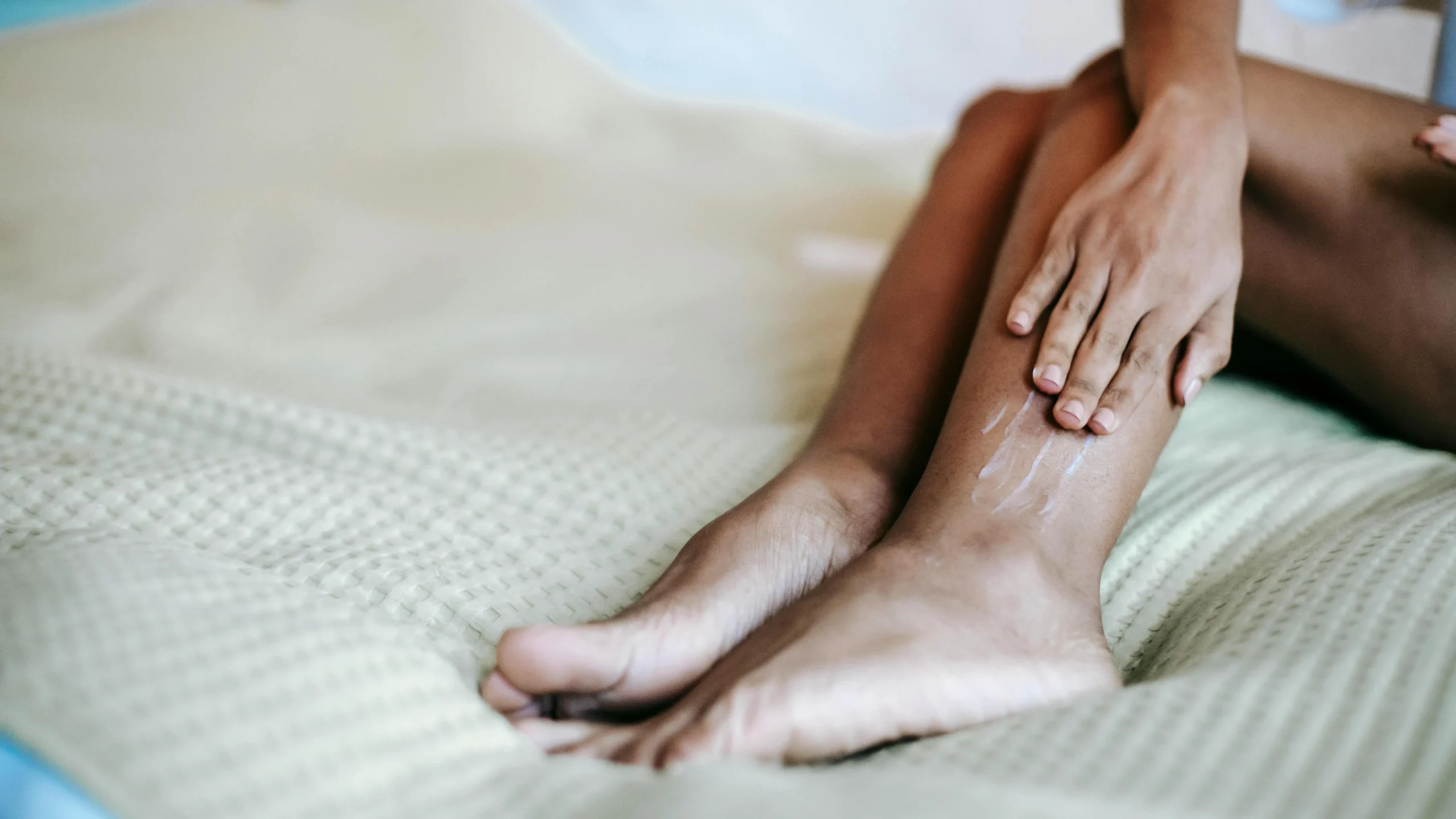 Woman moisturizing chafed skin on thighs while sitting on a bed.