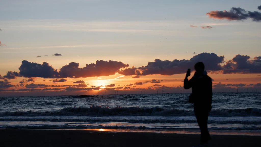 Woman experiencing heat rash between breasts while standing on the beach at sunset