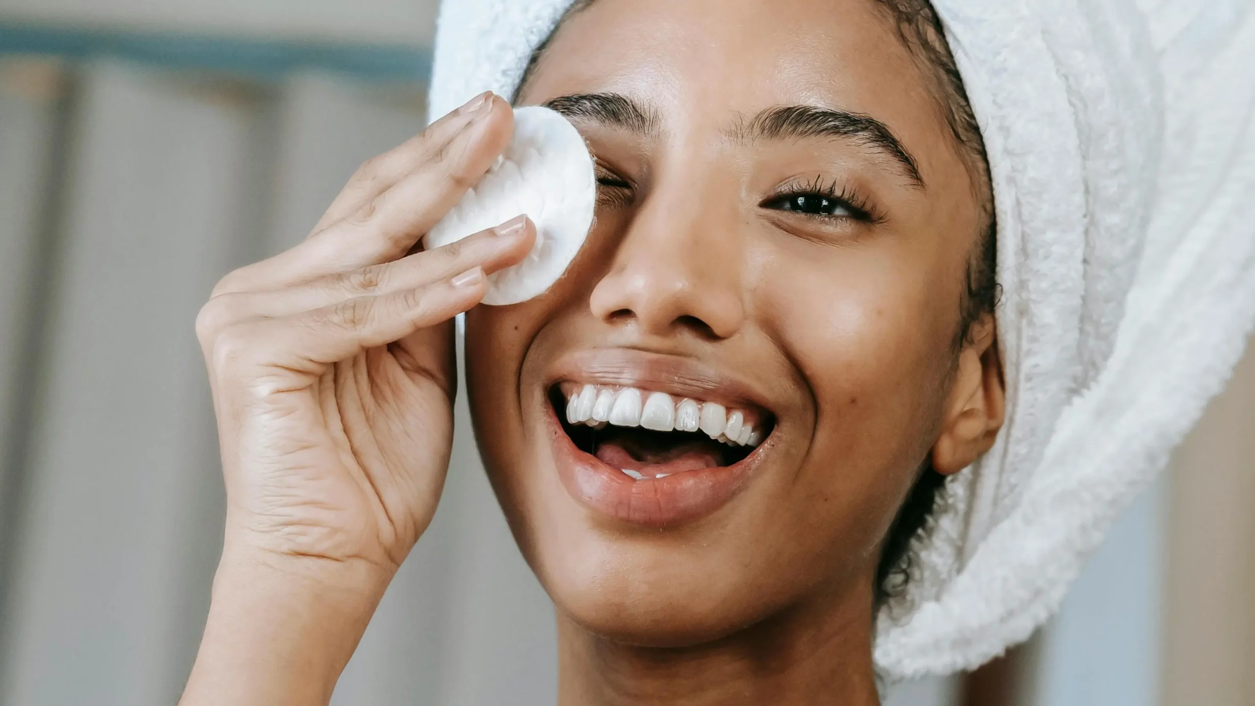 Smiling woman with towel turban applying lotion, illustrating how to stop vaginal odor.