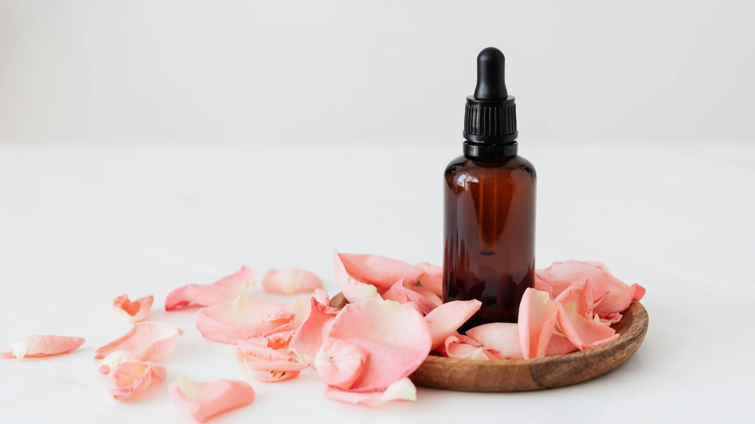 Rose petals with dark glass essence flask, symbolizing treatment for ingrown hair on vag.