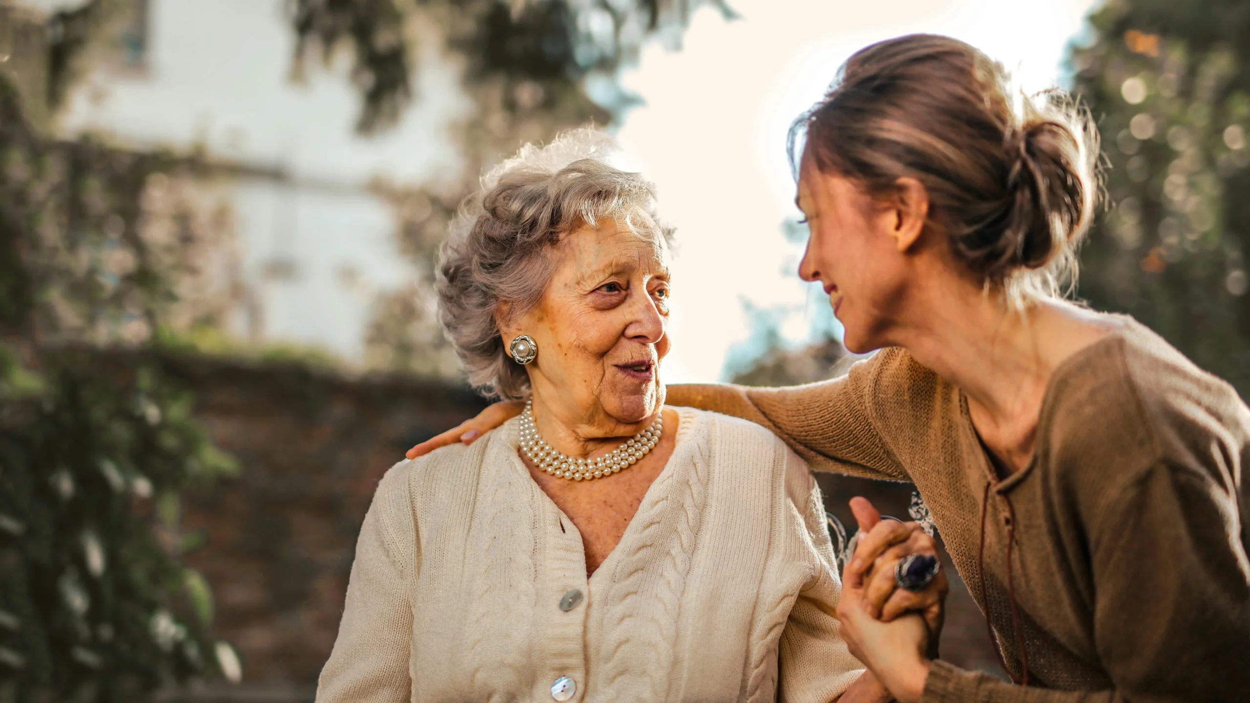 Adult daughter joyfully greeting surprised senior mother in garden