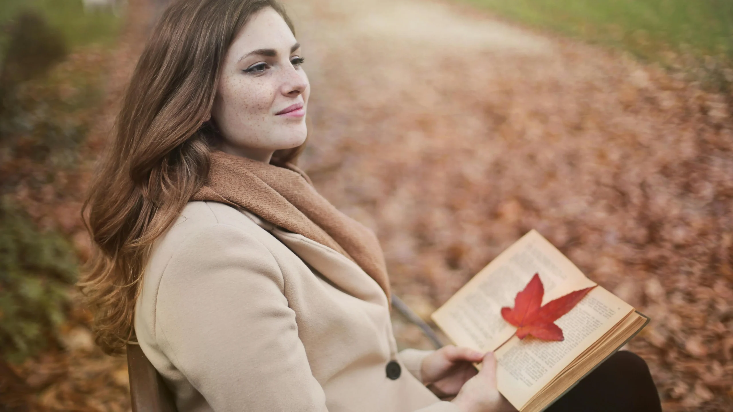 Young woman in autumn park reflecting on perimenopause symptoms with an open book