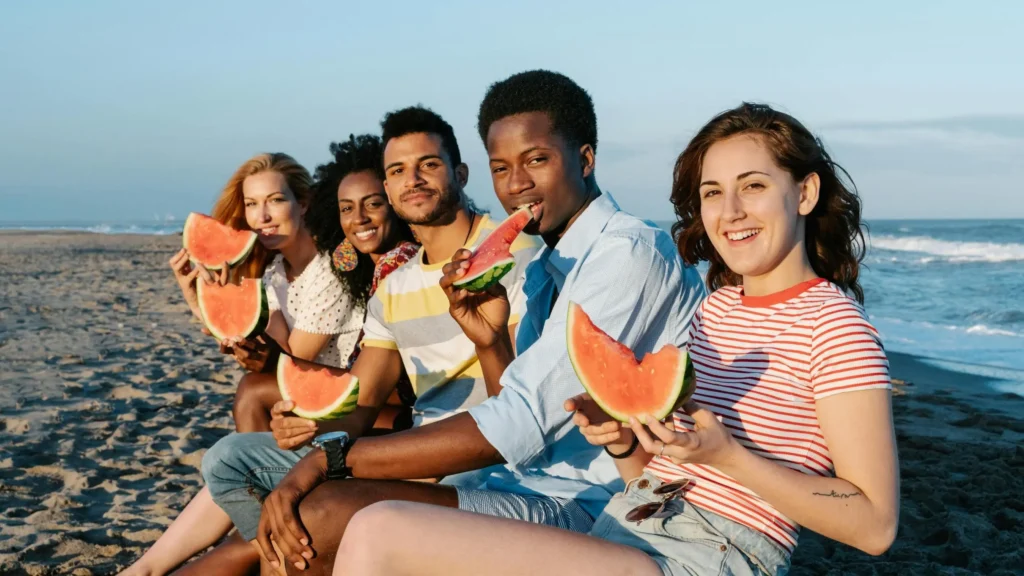 Friends enjoying watermelon on the beach in shorts for chub rub.