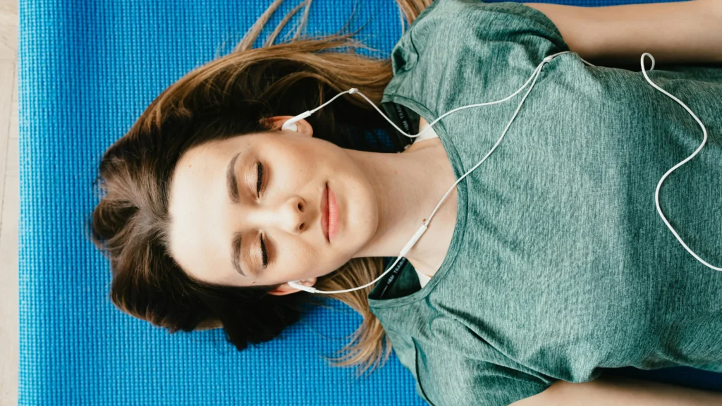 Woman on yoga mat relaxing with earphones, managing vaginal dryness itching