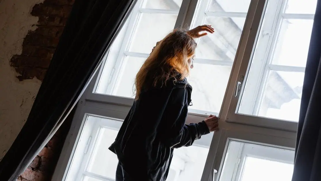 Woman experiencing breast pain during menopause, looking outside a window.