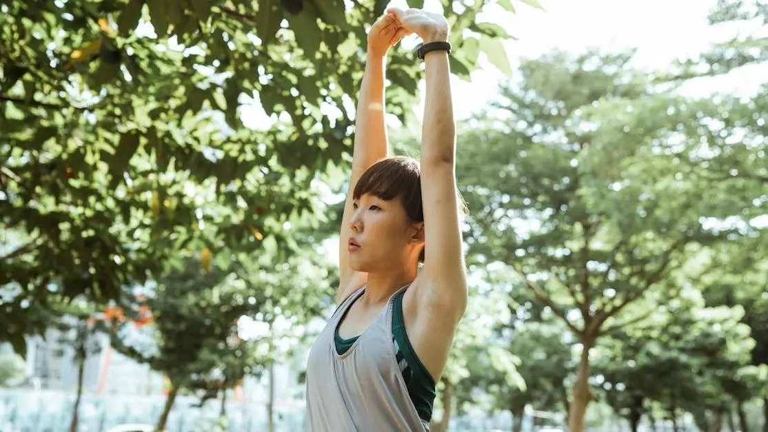 Asian woman in sportswear stretching arms in park on a sunny day, illustrating how to get rid of menopause belly