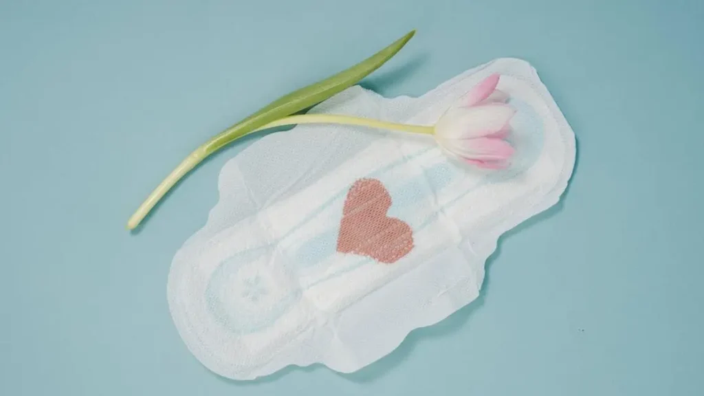 Feminine pad and pink tulip on blue background, relating to "i can smell my discharge through my pants".