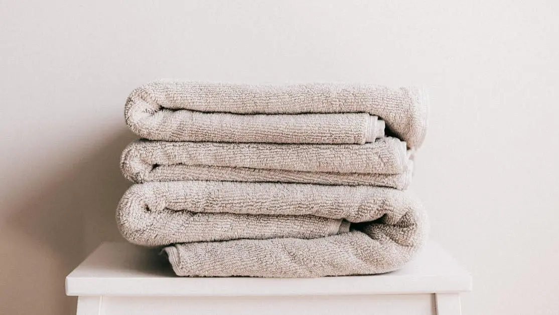 Stack of clean folded beige towels on a white stool, "I can smell myself through my pants" article cover photo