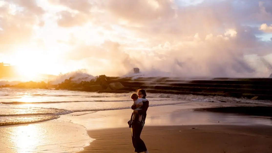 Mother holding baby on the seashore at sunset highlighting postpartum vaginal dryness issues