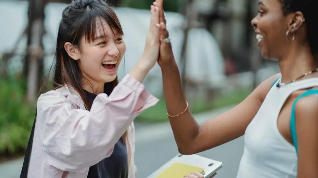 Excited multiracial female students high-fiving in park to prevent thigh chafing during breaks