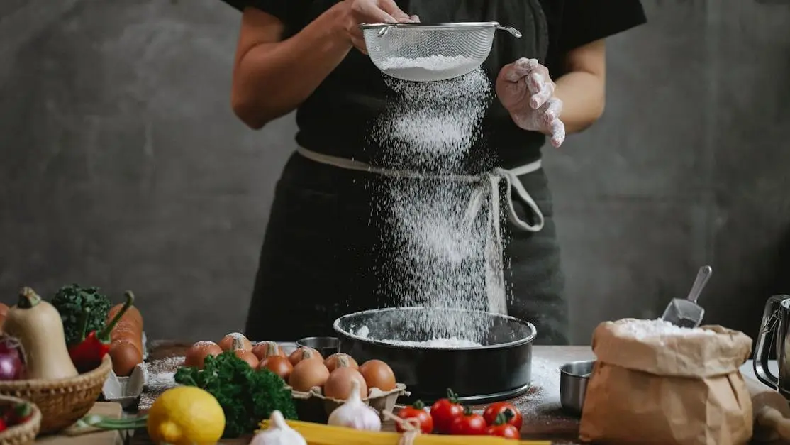 Cook adding flour into baking dish with spaghetti, cherry tomatoes, garlic, herbs, and lemon for Baking Soda BV