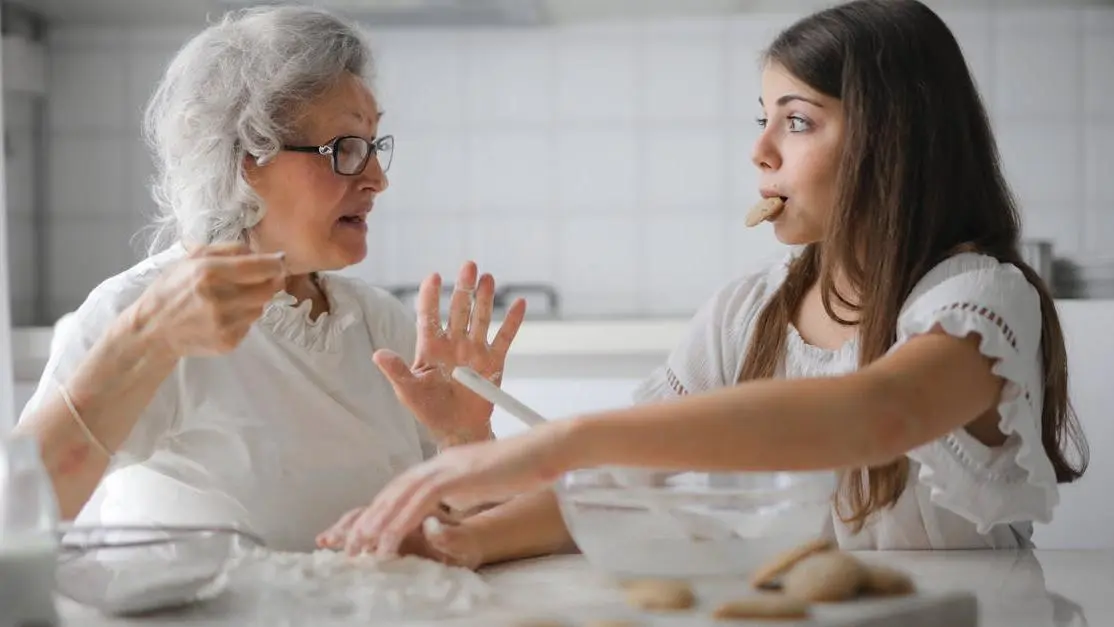 Senior woman discussing diagnosing menopause with teenage girl while cooking in modern kitchen.