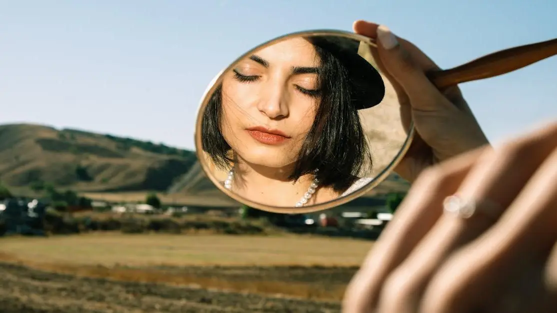 Young woman examining her face with a small mirror, highlighting signs for diagnosing peri menopause