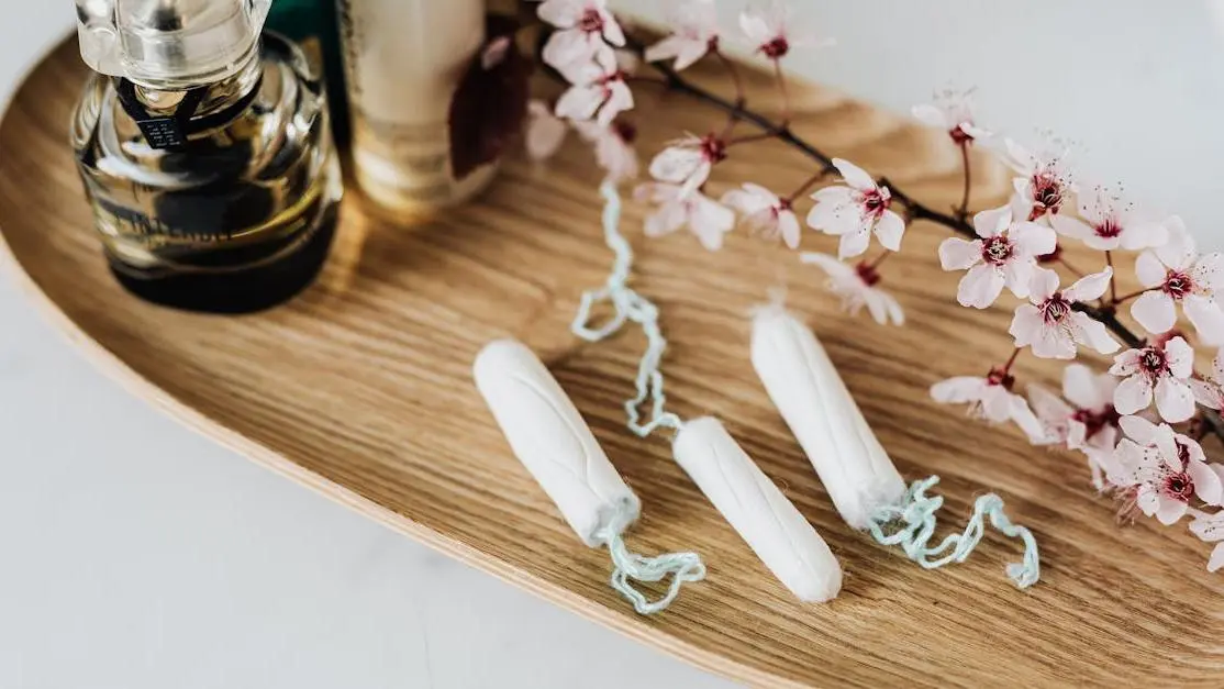 Feminine hygiene kit with perfume, cosmetic products, tampons, and a flower branch on a wooden tray