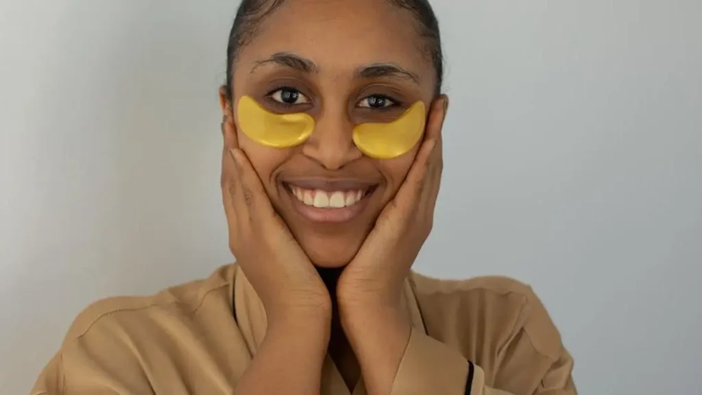 African American woman in bathrobe with soothing eye patches smiling, representing relief for heat rash underboob