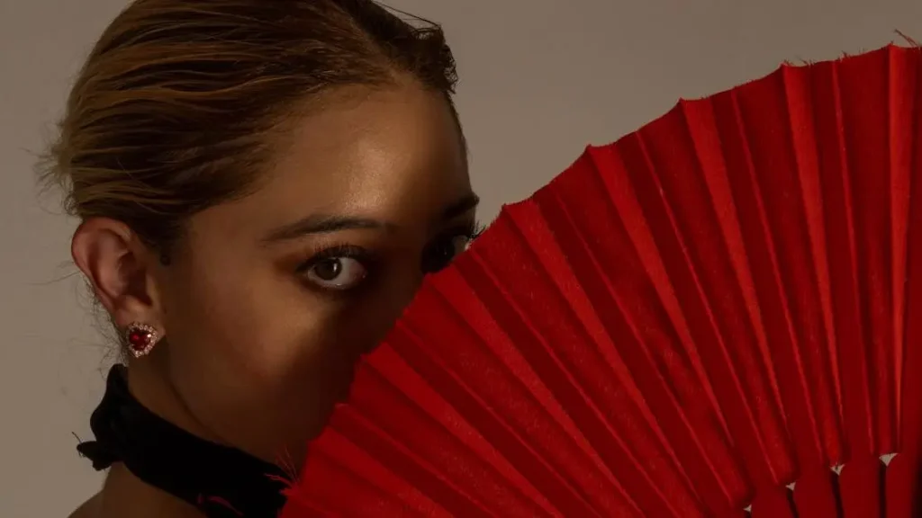 Woman managing hot flashes related to breast cancer with a red fan