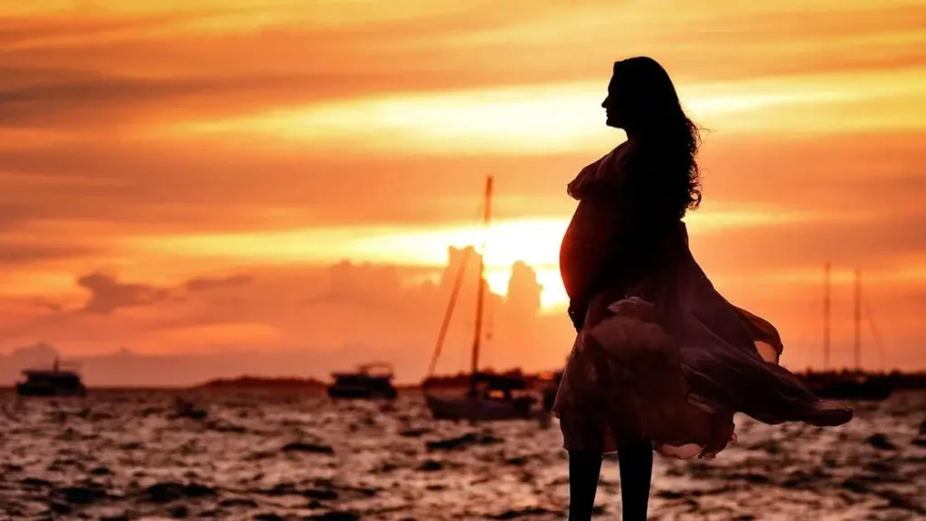 Pregnant woman experiencing hot flashes near seashore at sunset.