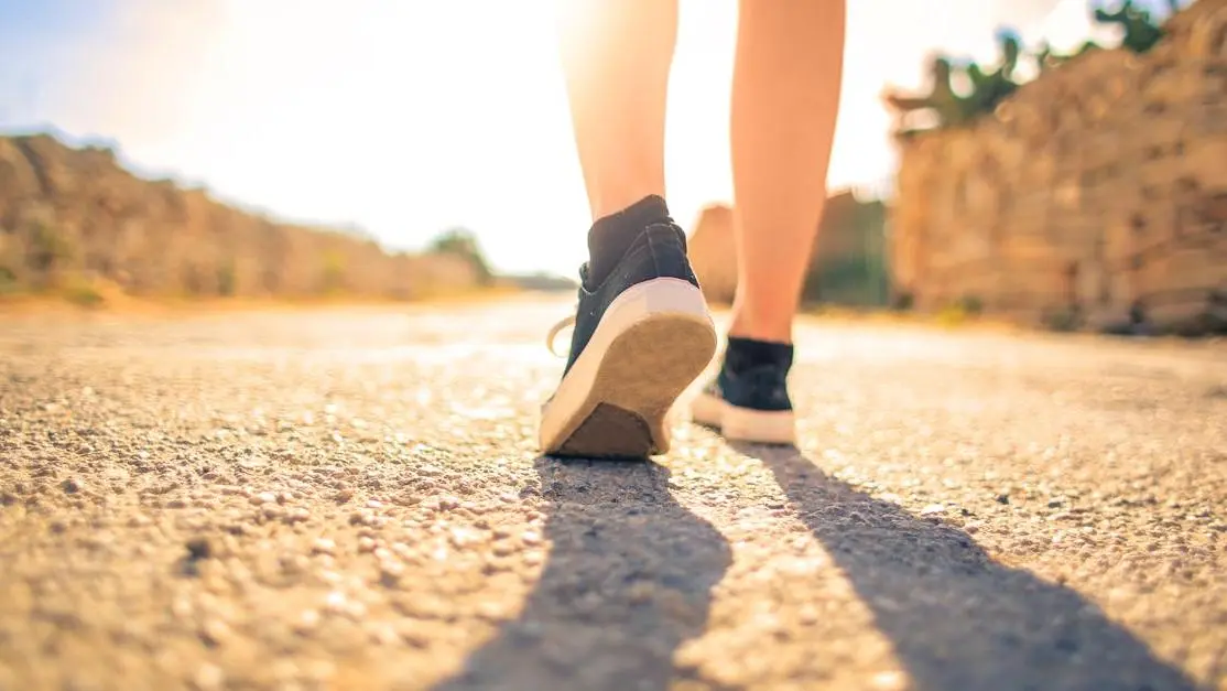 Woman experiencing hot flashes due to PCOS while walking on a sunny pathway