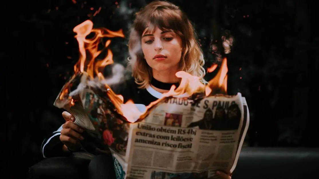 Young woman reading a burning newspaper symbolizing hot flashes in younger women.