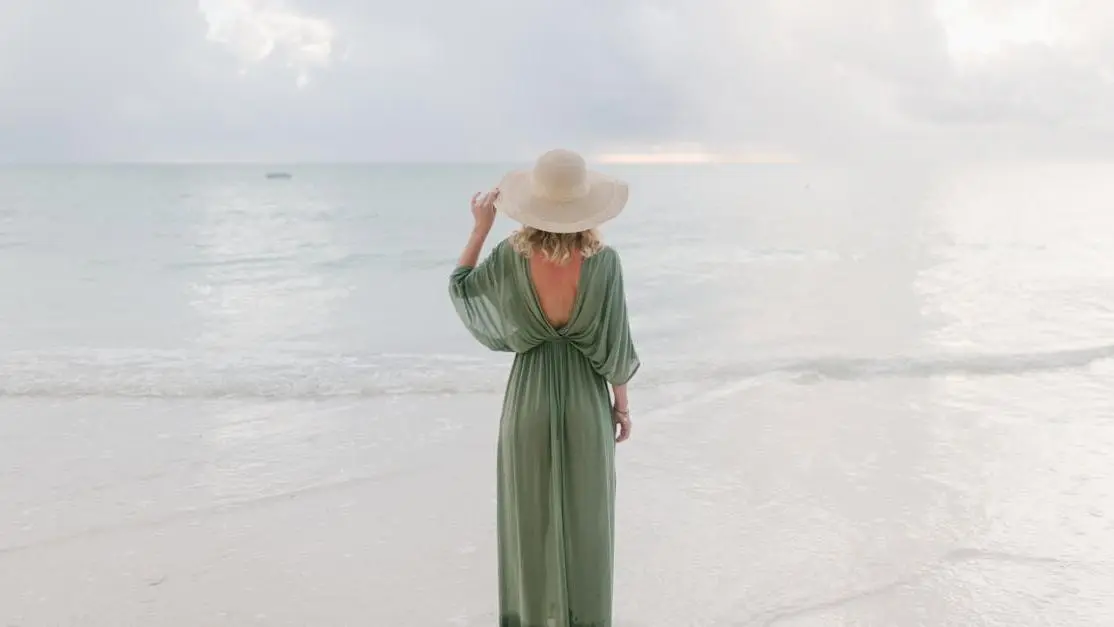 Woman in summer dress and hat standing on beach, symbolizing relaxation during irritable bladder menopause.