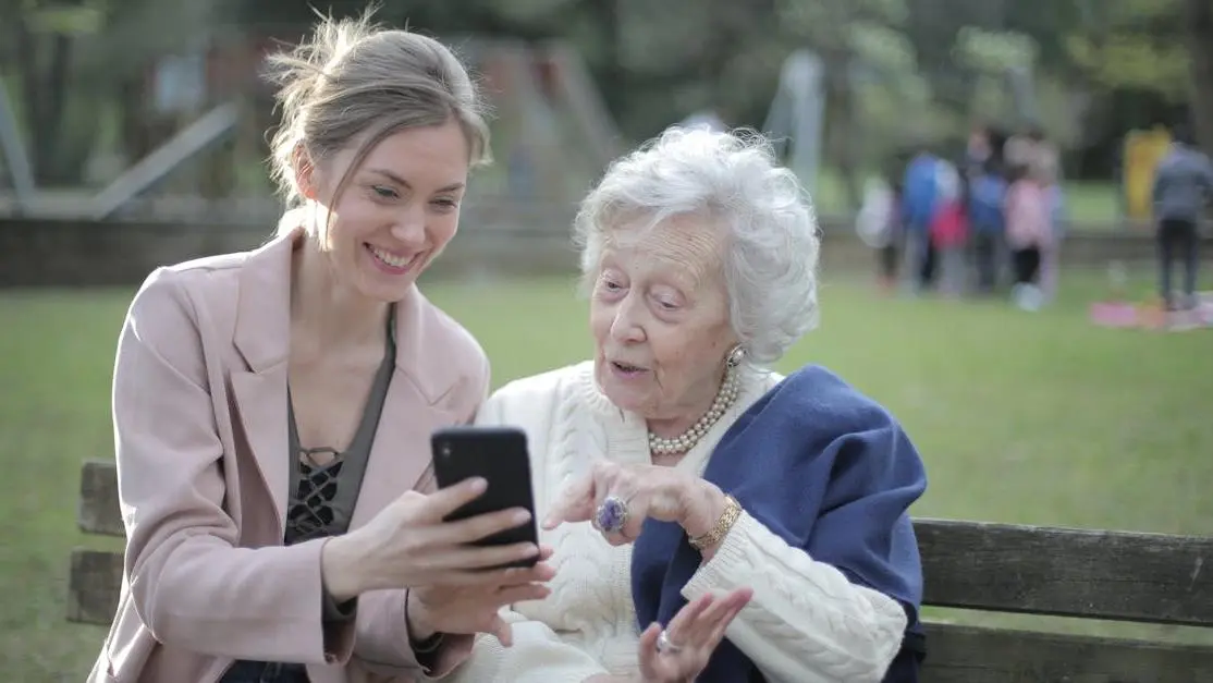 Happy female relatives on park bench learning about Menopause FAQs on a mobile phone.