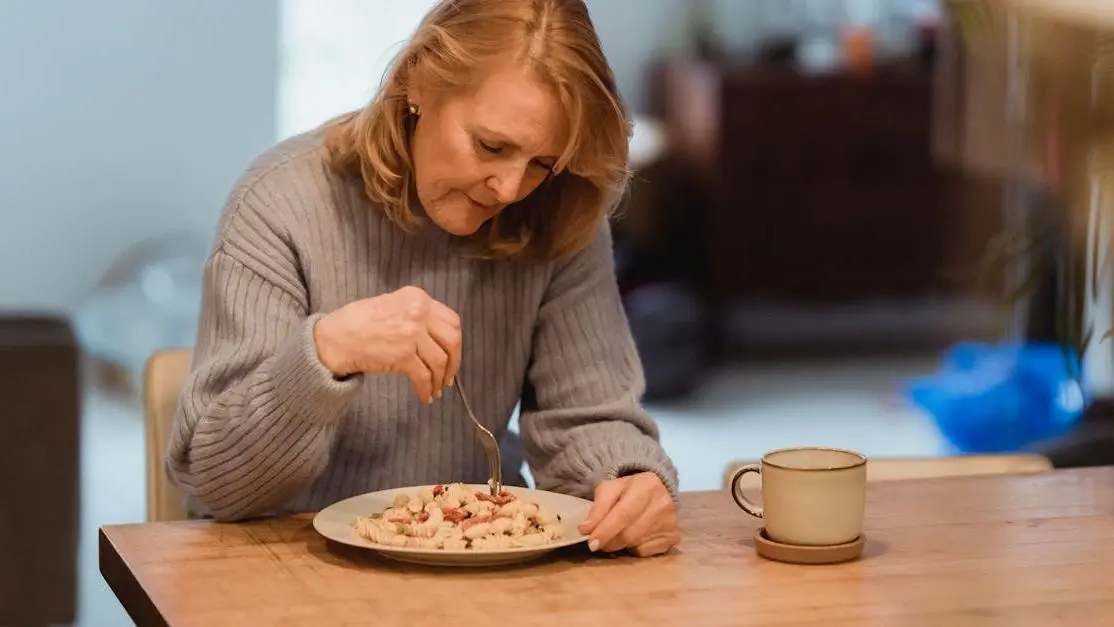 Senior woman in blue sweater experiencing menopause hot flashes after eating vegetable pasta