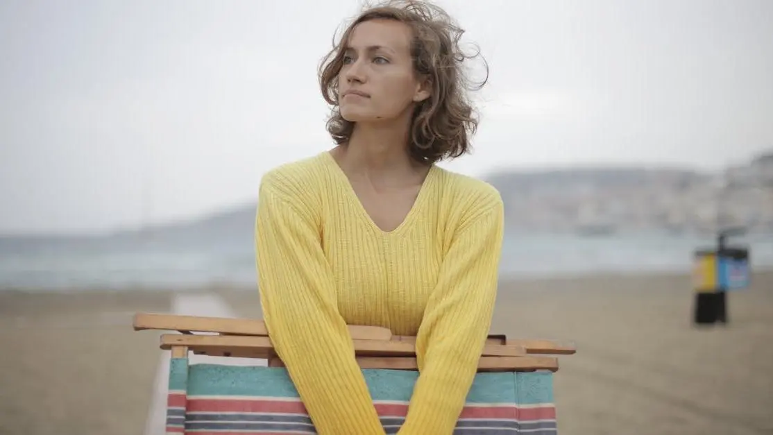 Woman with folded deckchair on overcast beach, symbolizing the isolation felt during peri menopause hot flashes