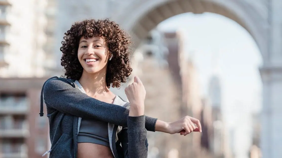 Young woman with Afro curls in sportswear stretching, listening to music, preventing sweat rash from sports bra