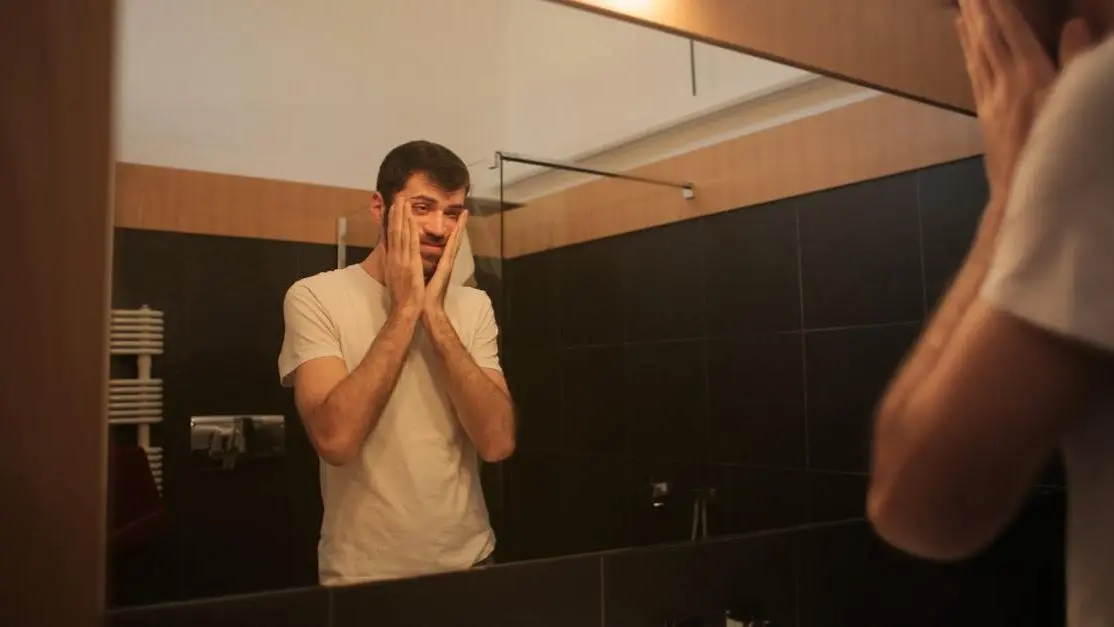 Man examining sweat rash in between breasts in bathroom mirror