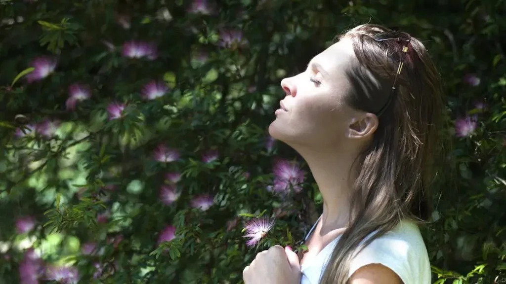 Woman shielding eyes from sunlight near purple flowers, illustrating sweat rash prevention.