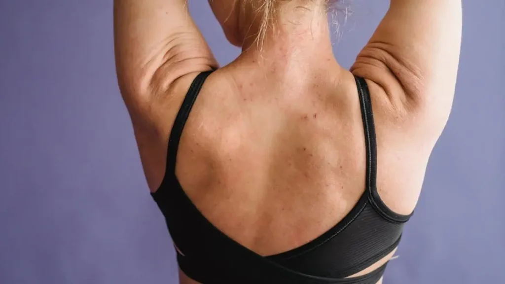 Muscular woman with sweat rash under sports bra against a purple background