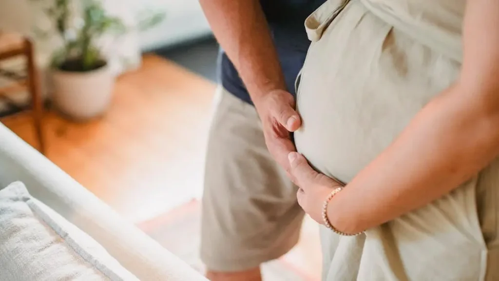 Pregnant woman with sweat rash under stomach gently touched by partner in light living room