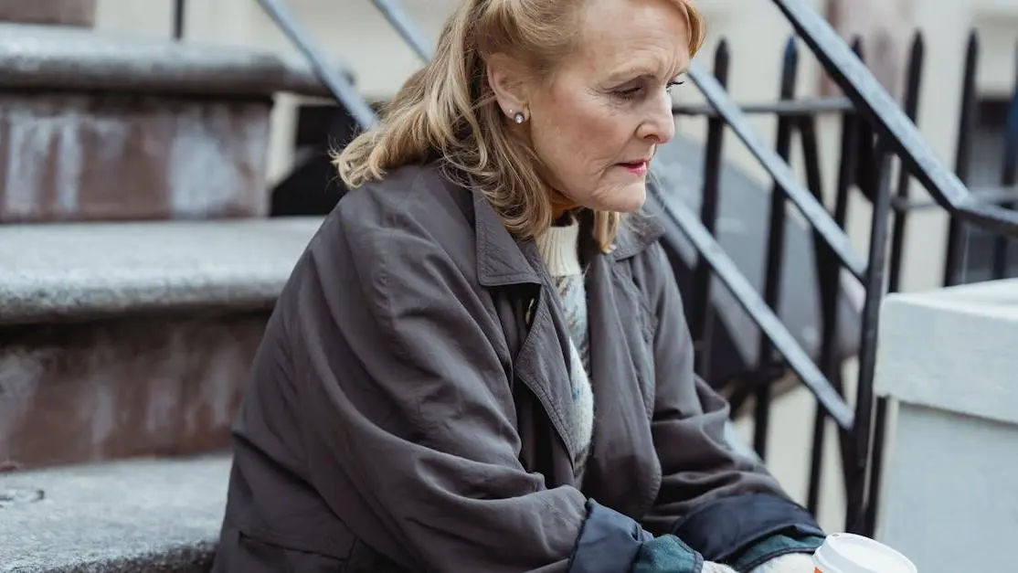 Senior woman with wrinkles and aging skin experiencing menopause, sitting on city stairs with a hot drink