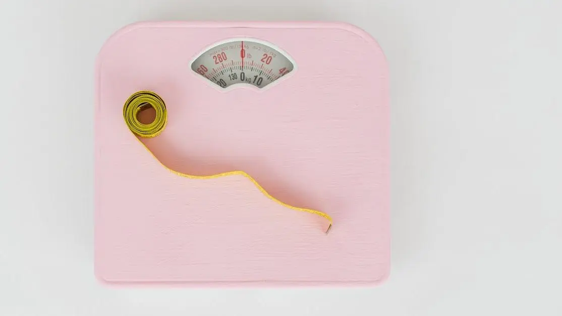 Pink weighing scale and yellow measuring tape representing GLP-1 Weight Loss Program.